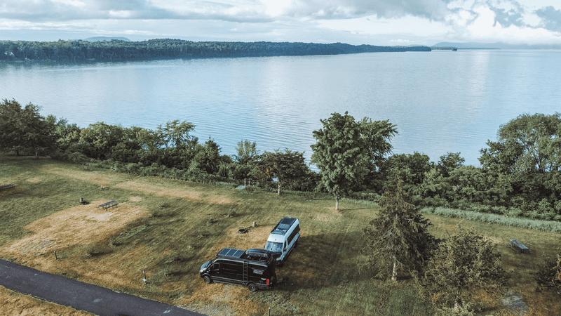 Two vans seen from above next to a lake with mountains in the background in the summer.