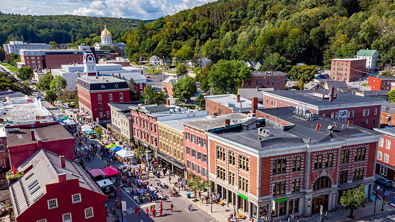 Seen from above, a vibrant town center with a parade of people walking down the main street on a sunny day.