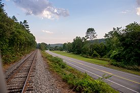 A railroad track and a paved automobile road parallel each other into the distance on a summer day.