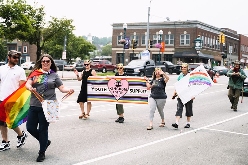 People walk down a street as part of a parade on a warm day.