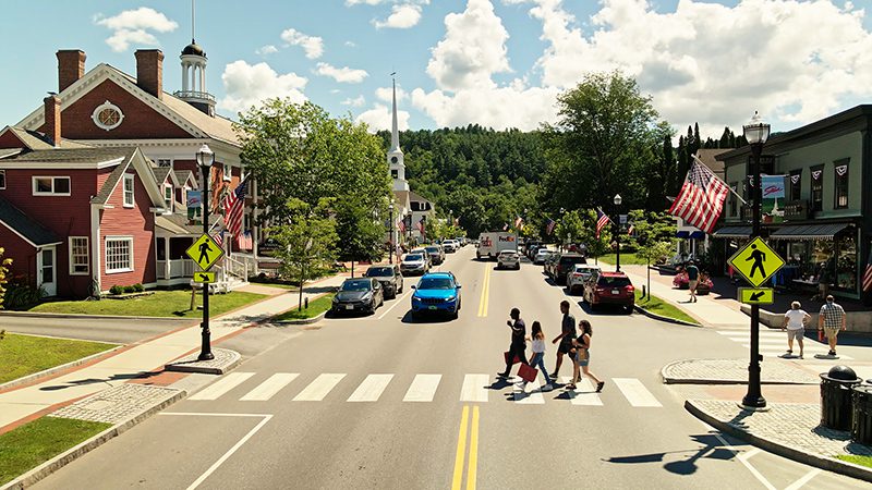 Four people use a crosswalk to cross the street on a sunny day.