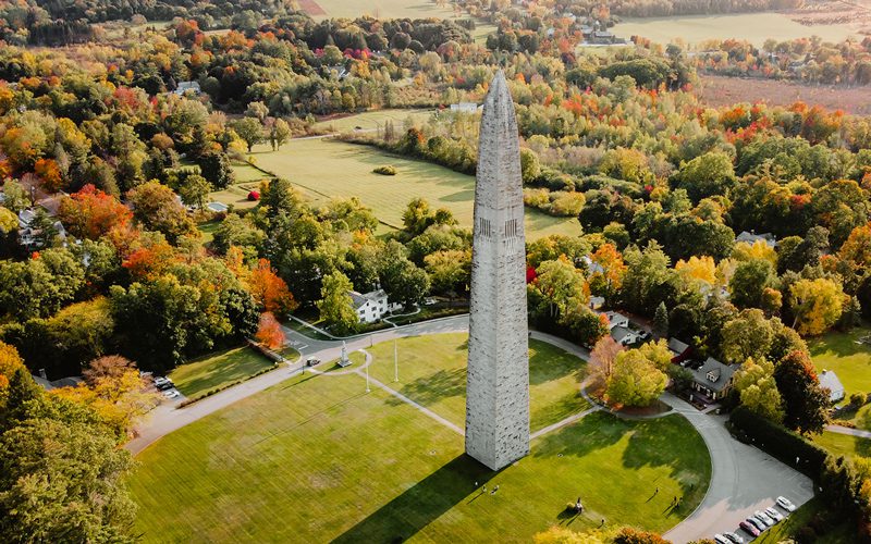 Seen from above, a tall stone monument surrounded by forests on a sunny day.