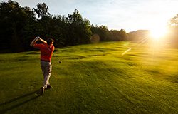 A person swinging a golf club at sunset.