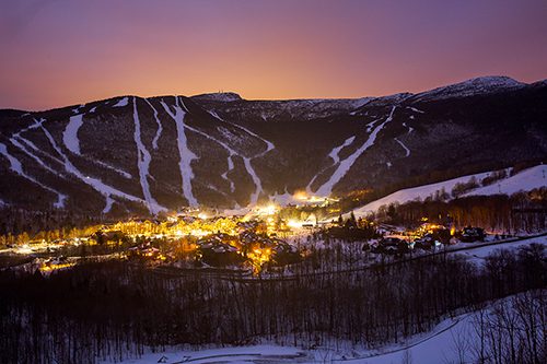 Seen from above, a lodge at the base of a mountain lit up at dusk.