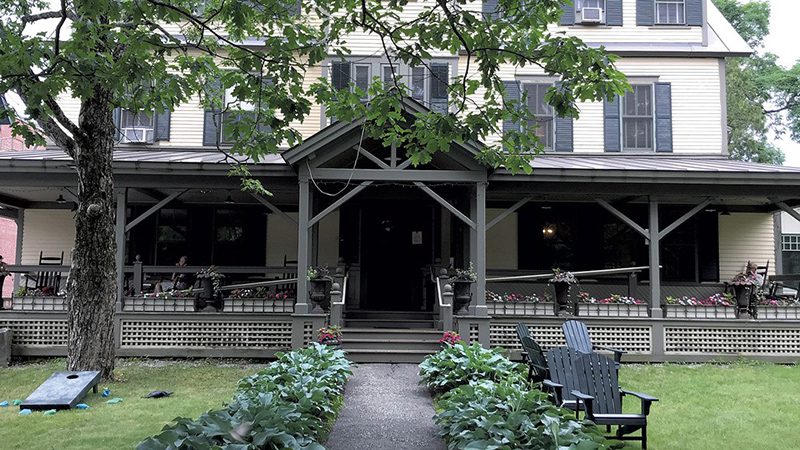 A historic building with timberframed accents and leafy plants lining a gravel walkway.