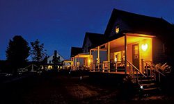 At dusk in the summer, a wooden cabin is lit with a soft warm glow.