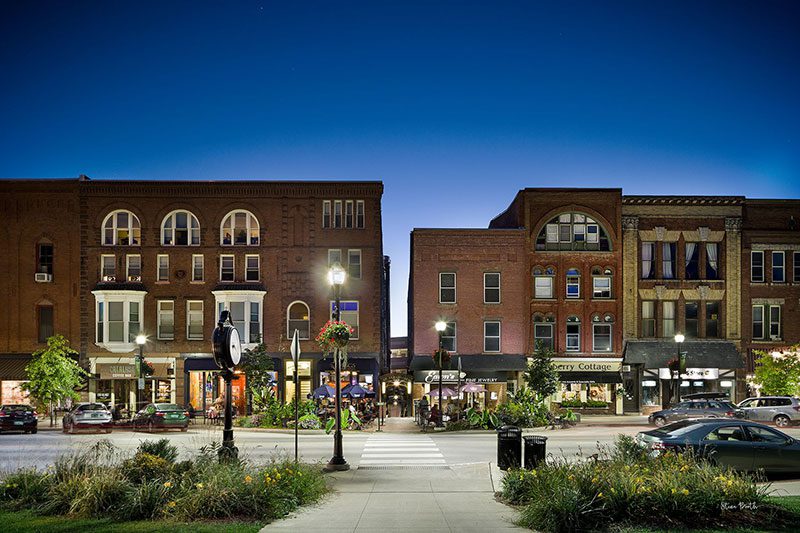 A row of brick buildings line a road with night lights at dusk.