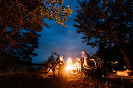 A person sits next to a campfire at night.