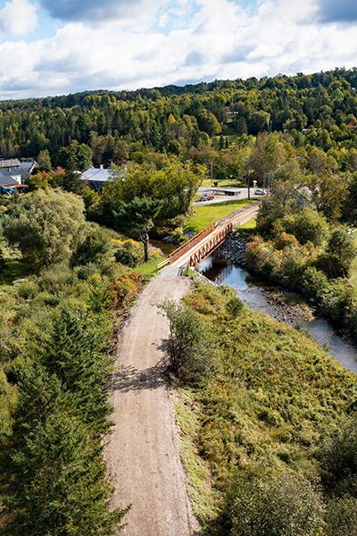 Seen from above, a gravel path with a bridge stretching across a river in summer.