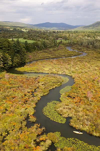 Seen from above, a person kayaks along a narrow, curving river.