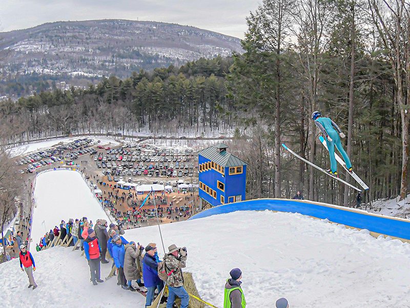 A person jumps off a high ski jump outdoors in winter.