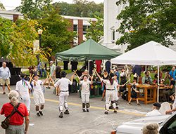 A group of people does a synchronized dance next to booth tents.