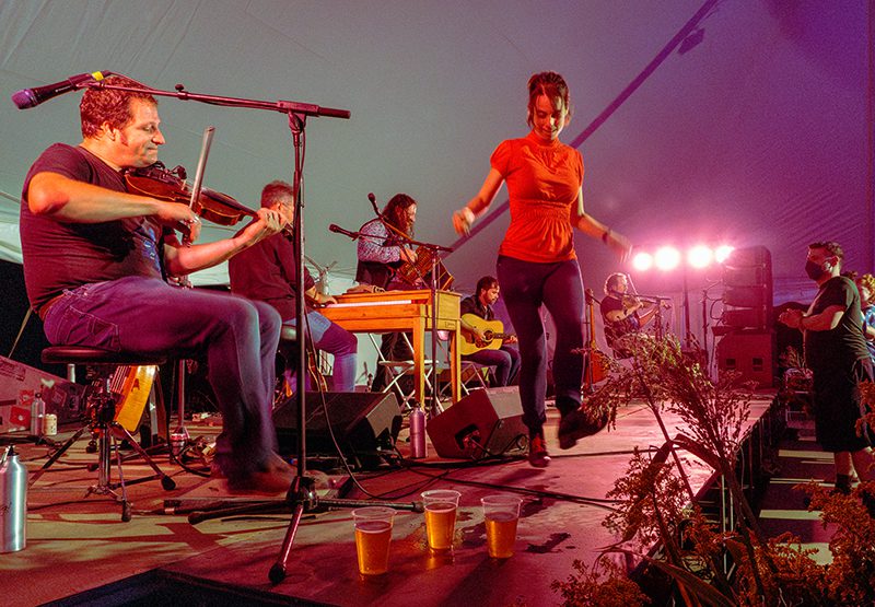 A person dances on stage while another person plays the violin.