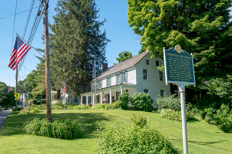 A Constitution House historic marker with a historic white house behind it.