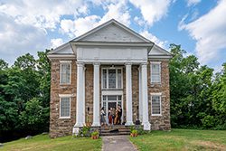 A group of musicians play music together on the porch of a historic stone house.