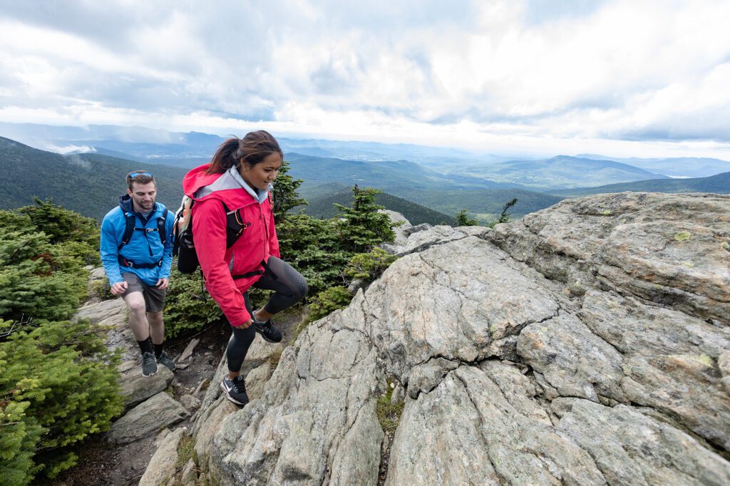 Two people hike up a rocky path at the top of a mountain.